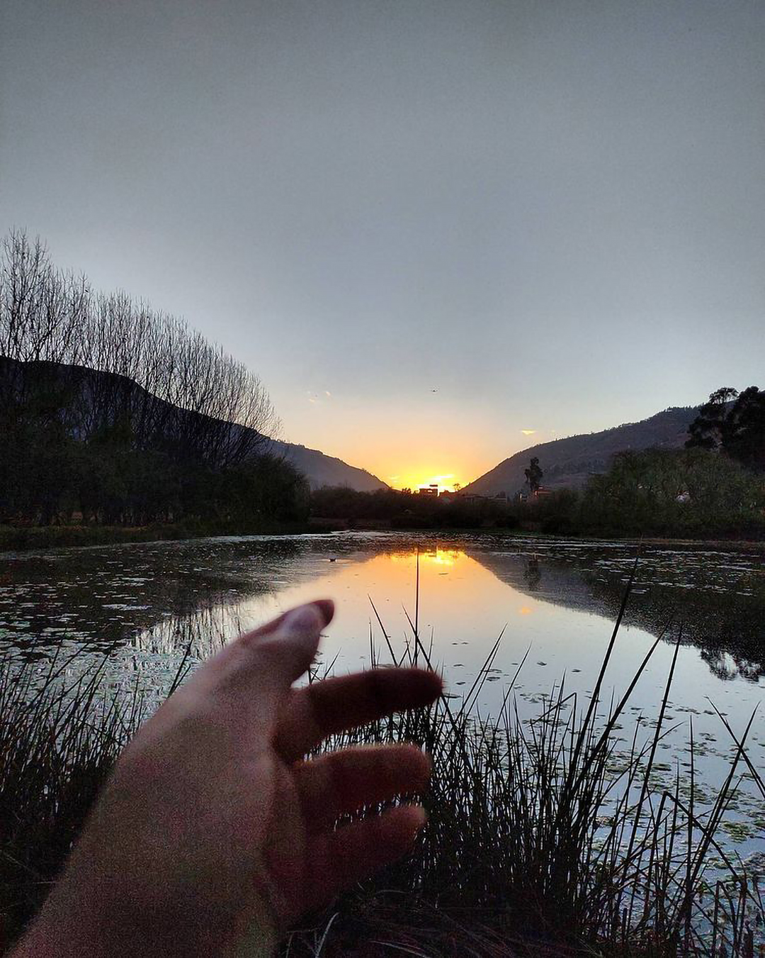 Atardecer en el Humedal de Huasao, una mano simula alcanzar el ocaso