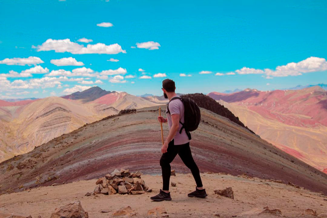 Hombre caminando bajo un cielo azul sobre vinicunca, montaña del Perú